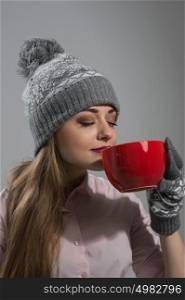 Woman in winter clothes enjoying a hot drink eyes closed on gray background