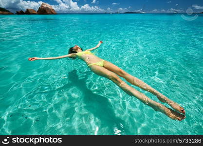 Woman in yellow bikini lying on water at tropical beach