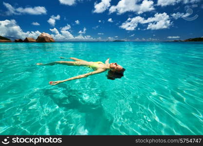 Woman in yellow bikini lying on water at tropical beach