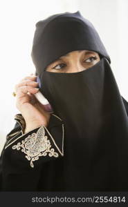 Woman indoors on cellular phone wearing veil (high key)