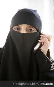 Woman indoors on cellular phone wearing veil (high key)