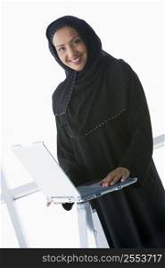 Woman indoors standing with laptop and smiling (high key/selective focus)