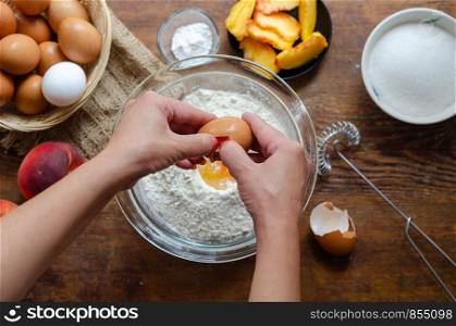 Woman is breaking eggs into flour. She is making peach pie.(