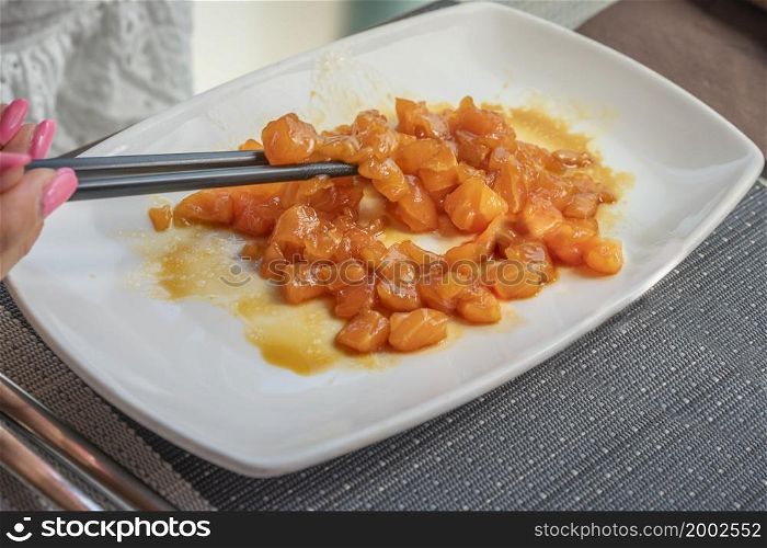 Woman is eating Salmon tartar on white dish with chopsticks