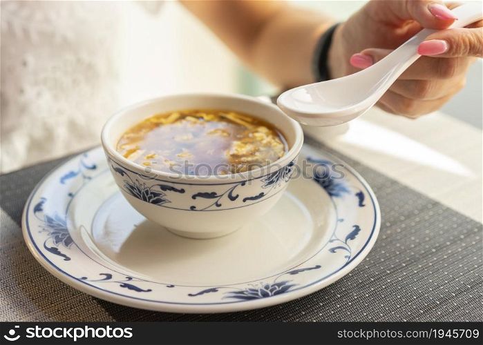 Woman is eating with ceramic spoon chinese vegetable soup at the restaurant