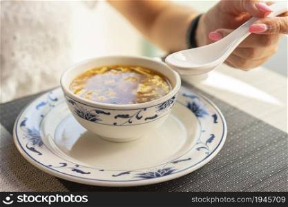 Woman is eating with ceramic spoon chinese vegetable soup at the restaurant