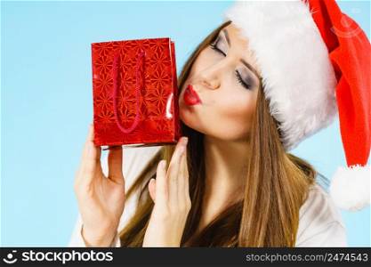 Woman is happy to give Christmas gifts. Female wearing santa claus hat holding present red gift bag, on blue. Happy Christmas woman holds red gift bag