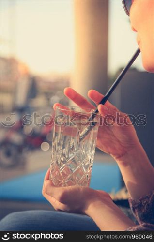 Woman is holding a glass with clear beverage and ice cubes