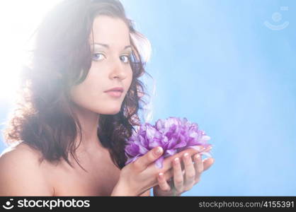 woman is holding purple flower in hands at sunny weather on blue background