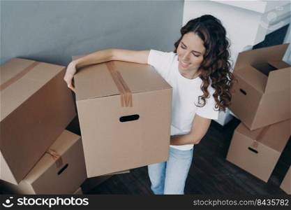 Woman is moving to better place and carrying box. Happy european girl purchasing real estate. Lady is unloading cardboard boxes in living room. Changes and new life concept.. Woman is moving to better place and carrying box. Happy european lady purchasing real estate.