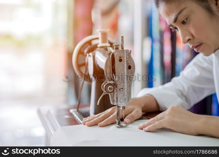 woman is sewing with sewing machine at home while sitting at her working place