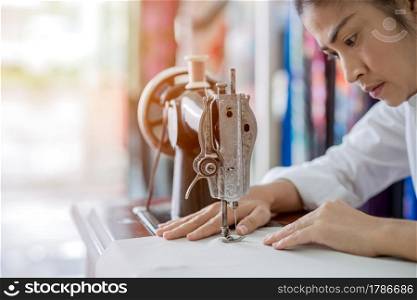 woman is sewing with sewing machine at home while sitting at her working place