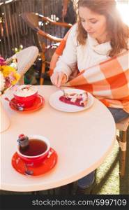 Woman is sitting in cafe outdoor and eat cake and cocoa, cozy autumn
