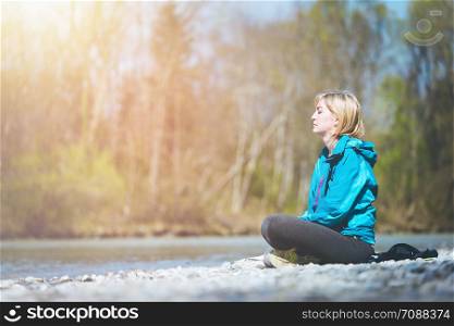 Woman is sitting on a pebble beach and doing meditation. Morning sun.