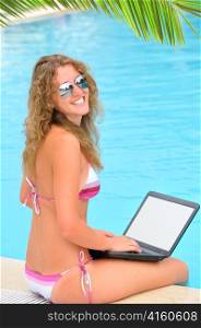 woman is sitting on the edge of swimming pool with laptop
