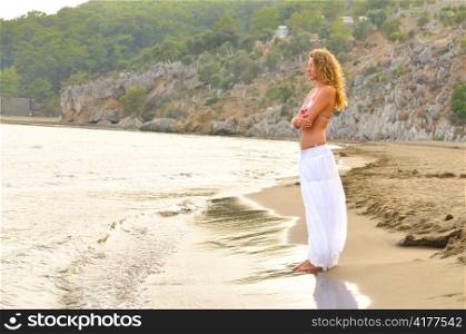 woman is standing alone on sea coast at sunset