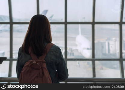 Woman is standing near window at airport. she is looking outside and observing transport. Copy space in right side.