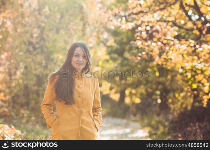 Woman is walking in autumnal park in yellow coat. Woman in autumnal park