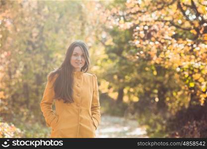 Woman is walking in autumnal park in yellow coat. Woman in autumnal park