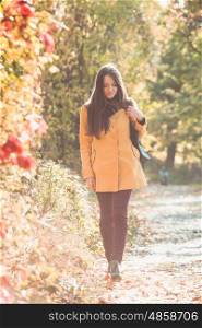 Woman is walking in autumnal park in yellow coat. Woman in autumnal park