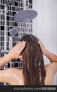 woman is washing her hair and face by rain shower head, rear view