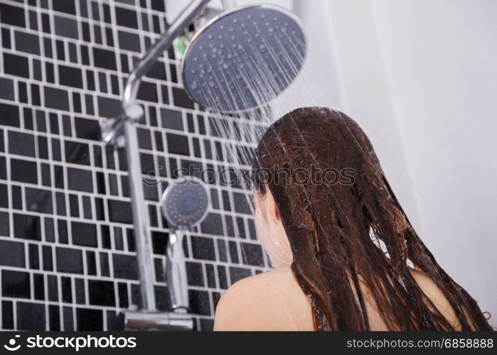 woman is washing her hair and face by rain shower head, rear view