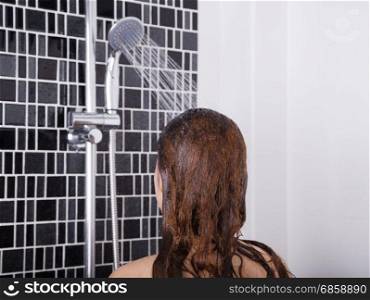 woman is washing her hair and face by shower head, rear view
