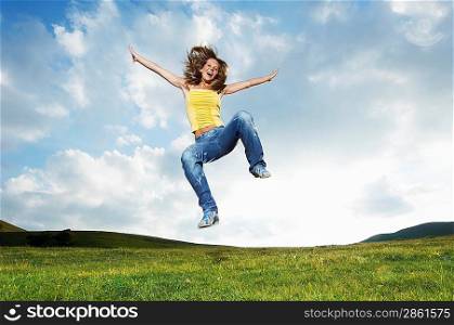 Woman jumping for joy in mountain meadow, front view