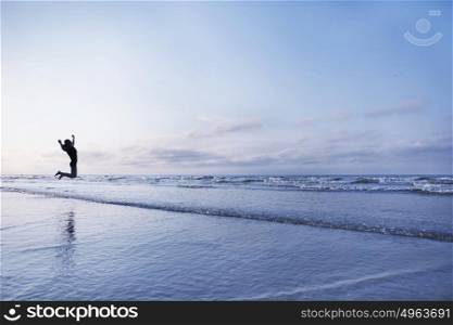 Woman jumping for joy on beach at sunrise