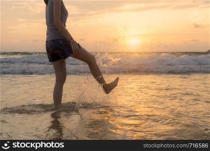 Woman kicking water at the beach during travel holidays vacation outdoors at ocean or nature sea at sunset time, Phuket, Thailand