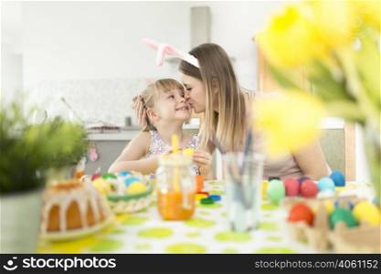 woman kissing daughter decorating easter eggs