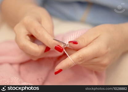 Woman knits with knitting needles light pink sweater from natural woolen threads wintertime