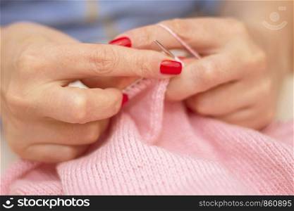 Woman knits with knitting needles light pink sweater from natural woolen threads wintertime