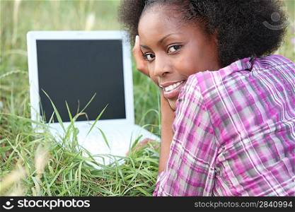 Woman laid in field in front of laptop computer