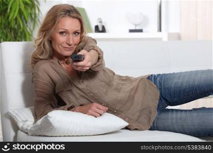 Woman laid on couch holding television remote control