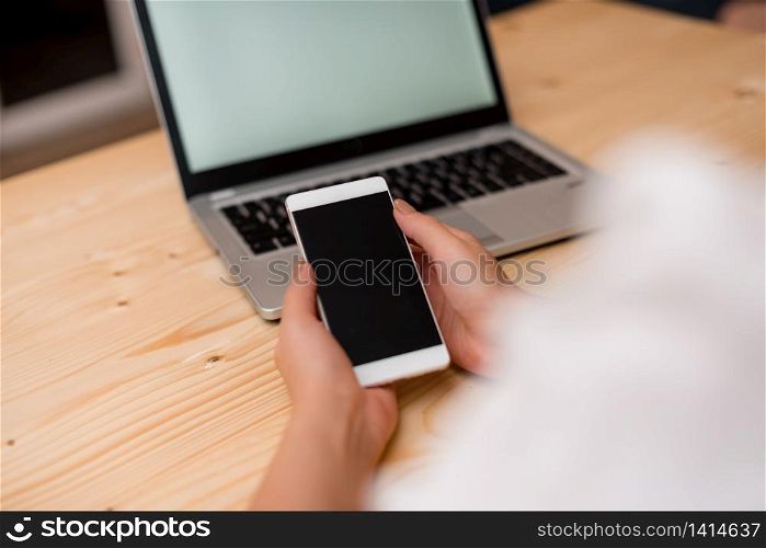 woman laptop computer smartphone mug office supplies technological devices. Young lady holding a smartphone with both hands. Gray laptop computer on the background with black keyboard. Office supplies, technological devices and wooden desk.