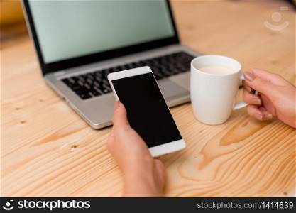 woman laptop computer smartphone mug office supplies technological devices. Young lady holding a smartphone and a cup of coffee or tea. Gray laptop computer on the background with black keyboard. Office supplies, technological devices and wooden desk.