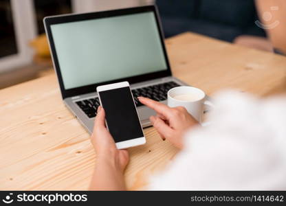 woman laptop computer smartphone mug office supplies technological devices. Young using a smartphone and pointing to the screen. Gray laptop computer on the background with black keyboard and coffee. Office supplies, technological devices and wooden desk.