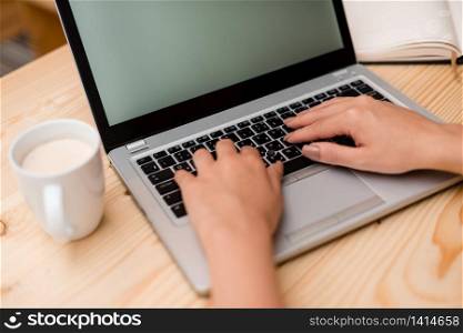 woman laptop computer smartphone mug office supplies technological devices. Young lady using a gray laptop computer and typing in the black keyboard with a mug of coffee or tea in the background. Office supplies, technological devices and wooden desk.