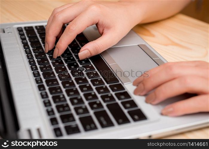 woman laptop computer smartphone mug office supplies technological devices. Young lady using a gray laptop computer and typing in the black keyboard with both hands in a room. Office supplies, technological devices and wooden desk.