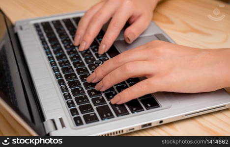 woman laptop computer smartphone mug office supplies technological devices. Young lady using a gray laptop computer and typing in the black keyboard with both hands in a room. Office supplies, technological devices and wooden desk.