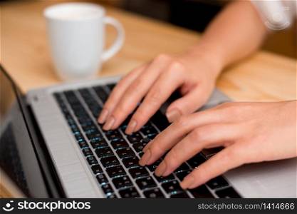 woman laptop computer smartphone mug office supplies technological devices. Young lady using a gray laptop computer and typing in the black keyboard with a mug of coffee or tea in the background. Office supplies, technological devices and wooden desk.