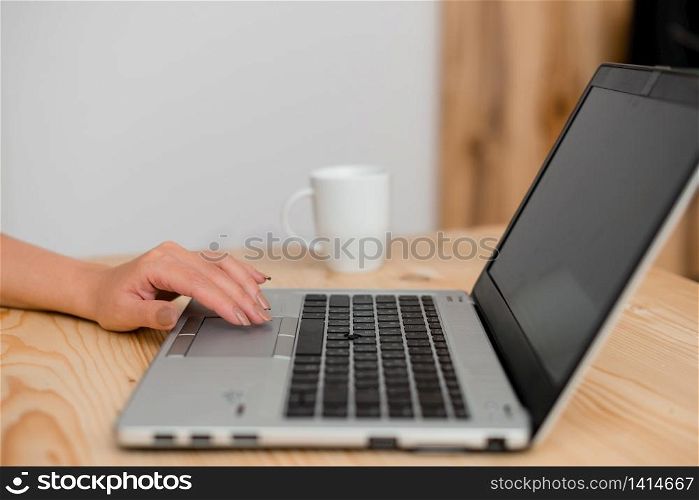 woman laptop computer smartphone mug office supplies technological devices. Young lady using a gray laptop computer and black keyboard with a hand on the touchpad. Mug of coffee in the background. Office supplies, technological devices and wooden desk.