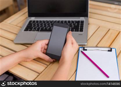 woman laptop computer smartphone office supplies technological devices. Young lady using and holding a dark smartphone in a crate table with a mug of black coffee. Office supplies, cell phone, technological devices and wooden desk.