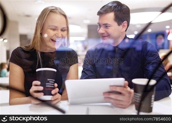 Woman laughs as man shows her something on his tablet as they sit on a table
