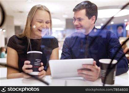 Woman laughs as man shows her something on his tablet as they sit on a table