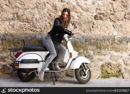 Woman launching a old scooter with pedal wearing casual clothes in urban background.