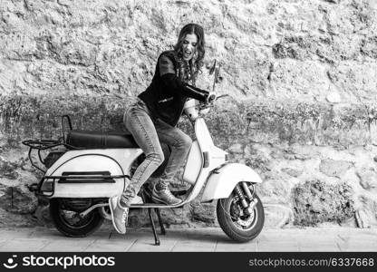 Woman launching a old scooter with pedal wearing casual clothes in urban background.