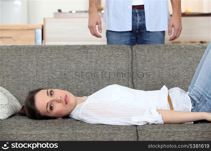 Woman laying on couch husband stood behind