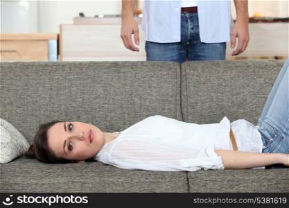 Woman laying on couch husband stood behind